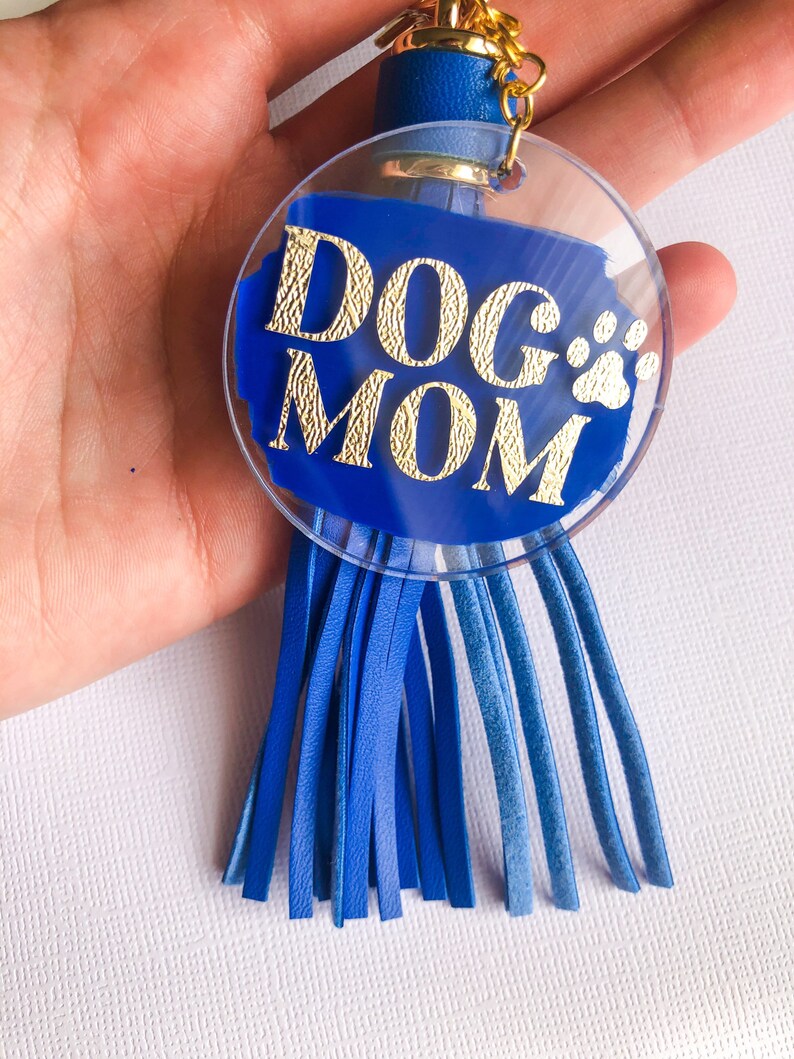 May include: Blue and gold keychain with a clear circle charm that says "DOG MOM" with a paw print. The charm is attached to a blue tassel.