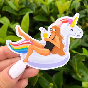 May include: A sticker of a woman wearing sunglasses and a black swimsuit, relaxing on a rainbow unicorn pool float with a yellow drink in her hand.