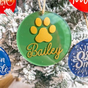 May include: Green round Christmas ornament with a gold paw print and the name "Bailey" written in gold script.