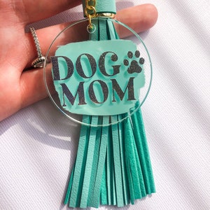 May include: A teal blue acrylic keychain with a silver glitter design that says "DOG MOM" with a paw print. The keychain has a teal blue tassel.