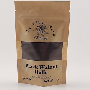 May include: A brown paper bag of black walnut hulls powder. The bag has a clear window showing the dark powder inside. Text on the bag reads "The Elder Herb Shoppe" and "Black Walnut Hulls (Juglans nigra) powder Net Wt. 1 oz."