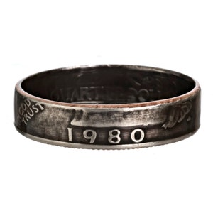 Puede incluir: Un anillo de plata hecho de un cuarto de dólar estadounidense de 1980. El anillo está desgastado y tiene una pátina de cobre en el interior.