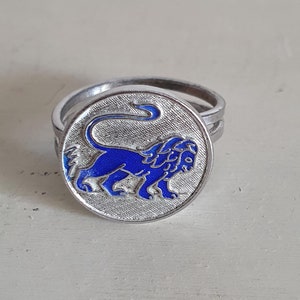 May include: A silver ring with a blue enamel lion design. The ring is a double band.