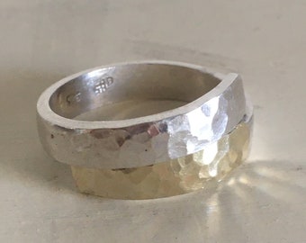 May include: A silver and gold hammered ring with a textured finish. The ring is marked "925" on the inside band.