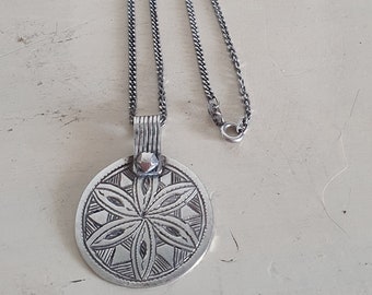 May include: A silver necklace with a round pendant featuring a detailed geometric design. The pendant is attached to a silver chain.