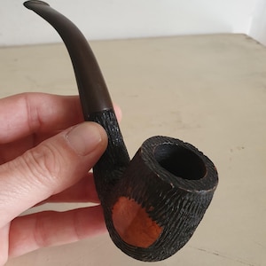 Peut inclure: Une pipe en bois noir avec un foyer brun et une tige incurvée. Le foyer a une surface texturée et un accent circulaire brun rougeâtre.