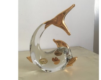 May include: A glass dolphin figurine with gold accents. The dolphin is in a jumping pose with its tail raised. The figurine has a label that reads "Murano Art Glass Italy".
