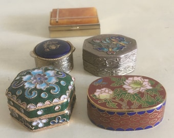 May include: Five small decorative boxes with intricate designs. The boxes are made of metal and have a variety of colors, including green, blue, red, and gold. The boxes are all closed and have a variety of floral and geometric patterns.