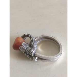 Peut inclure: Une bague en argent avec une pierre précieuse orange sertie dans un design détaillé. La bague est à double bande.
