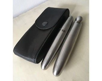 May include: Two silver metal tubes with a black leather case. The tubes have a rounded end and a flat end. The tubes have the letters "P1" engraved on them.