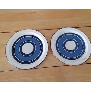 Könnte beinhalten: Zwei weiße Keramikplatten mit einem blauen konzentrischen Kreismuster. Die Teller haben einen gesprenkelten Rand und eine weiße Mitte. Die Teller liegen auf einer Holzoberfläche.