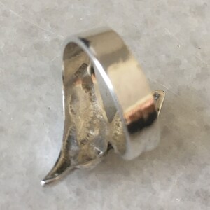 May include: Silver ring featuring a stylised bird design. The ring is open and has a smooth, polished finish.