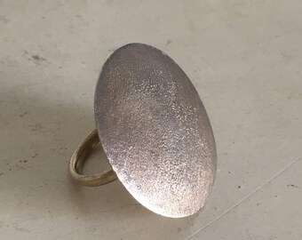 May include: A silver ring with a large, round, textured top. The ring is made of a thin band of metal.