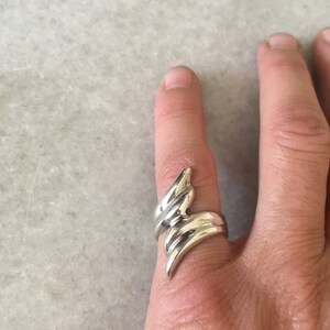 May include: A silver ring featuring a distinctive, abstract design. The ring is crafted from several curved bands that twist and turn, resulting in a dynamic and contemporary style.