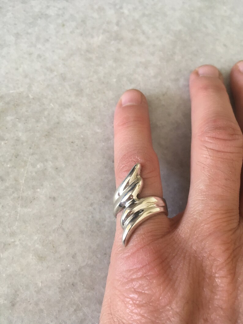 May include: A silver ring featuring a distinctive, abstract design. The ring is crafted from several curved bands that twist and turn, resulting in a dynamic and contemporary style.