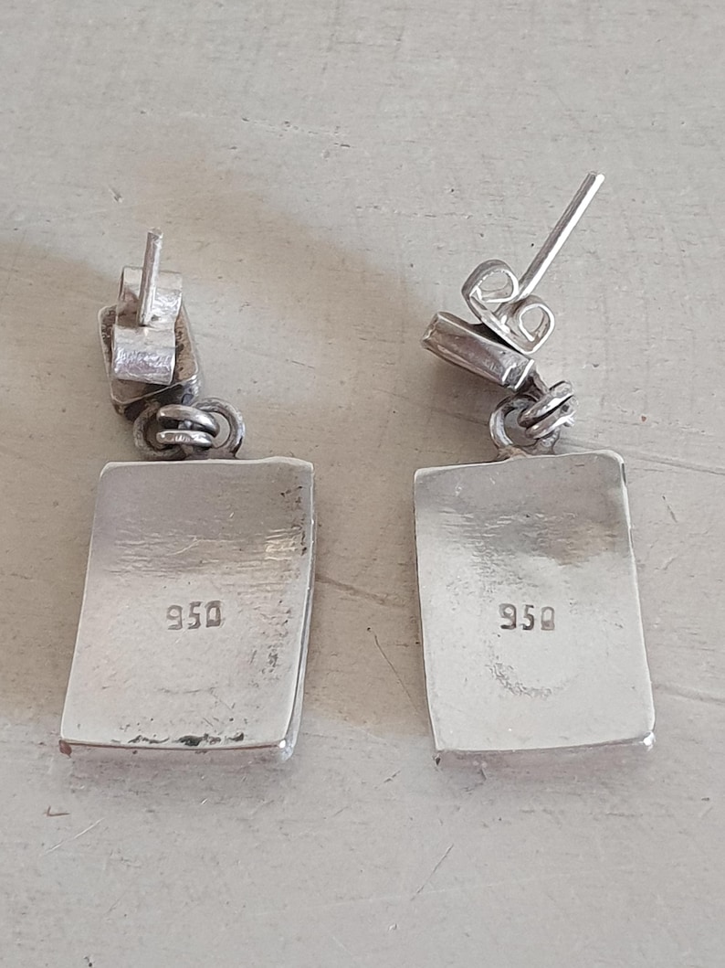May include: A pair of silver earrings with a rectangular shape and a 950 stamp on the back.