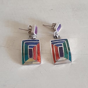May include: A pair of silver earrings with geometric designs. The earrings are made of silver and feature a variety of colorful stones, including turquoise, lapis lazuli, and coral.