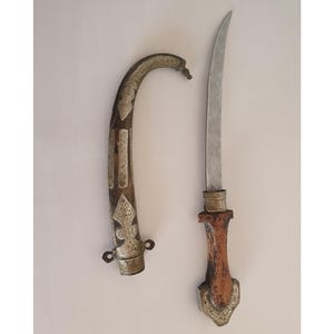 May include: An antique dagger with a curved, ornate handle and a silver blade. The handle is brown with silver accents and a decorative design. The sheath is curved and silver with a decorative pattern.
