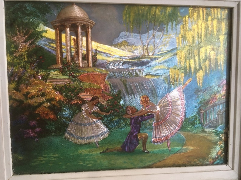 Op de afbeelding: Een vintage ingelijst kunstwerk dat een fantasierijke sc&egrave;ne met drie dansers in een tuinsetting toont. De dansers zijn gekleed in kleurrijke kostuums en voeren een balletroutine uit. De achtergrond toont een waterval, een prieel en weelderig groen.