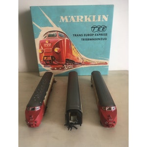Könnte beinhalten: Ein Vintage Marklin TEE Trans Europ Express Modellbahn-Set. Das Set enthält drei Waggons und eine Box mit einer Zugillustration. Die Waggons sind rot, schwarz und weiß.