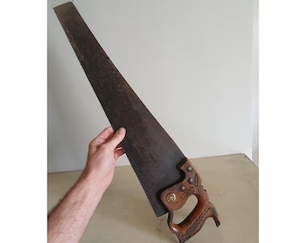 May include: A vintage hand saw with a wooden handle. The handle has a carved design and a brass accent. The saw blade is metal and has a slight curve.