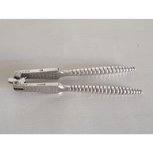 Peut inclure: Un casse-noix en métal argenté doté de deux poignées articulées avec un motif de prise nervuré et texturé, ainsi qu'une section centrale avec un petit motif circulaire alvéolé. L'outil possède un point de pivot à une extrémité et deux marques.
