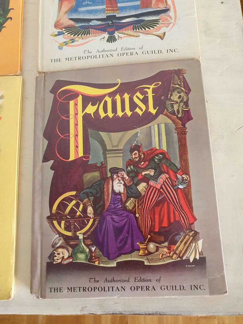 May include: A vintage book cover featuring an illustration of a man with a white beard and a red devil. The book title is "Faust" and the text "The Authorized Edition of THE METROPOLITAN OPERA GUILD, INC." is printed on the cover.