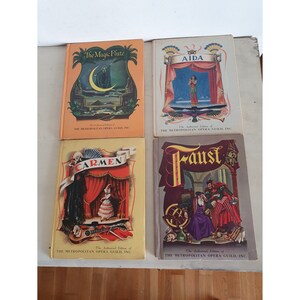 May include: Four vintage paperback books with colorful covers featuring illustrations of scenes from the operas The Magic Flute, Aida, Carmen, and Faust. Each book has the title of the opera printed on the cover in large, bold letters. The books are all published by The Metropolitan Opera Guild, Inc.