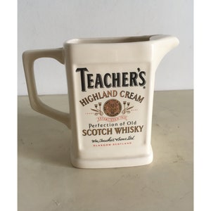 Op de afbeelding: Crèmekleurige keramische kan met een vierkante vorm en een handvat. De voorkant van de kan is voorzien van de tekst "Teacher's Highland Cream" en "Perfection of Old Scotch Whisky".
