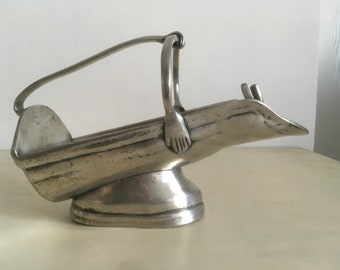 May include: A silver metal wine bottle holder with a handle shaped like a hand. The holder is designed to hold a bottle of wine horizontally.
