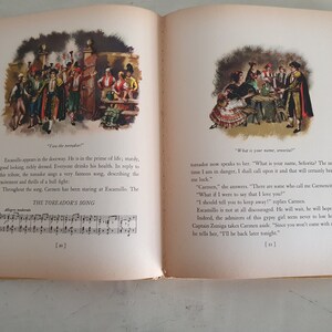 May include: An illustration from a children's book depicting a scene from the opera Carmen. The image shows a man in a red and gold costume singing to a woman in a red and black dress. The text in the image reads "What is your name, se&ntilde;orita?"
