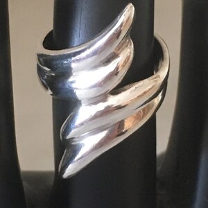 May include: A silver ring with a unique, abstract design. The ring is made of smooth, polished metal and has a modern, minimalist style.