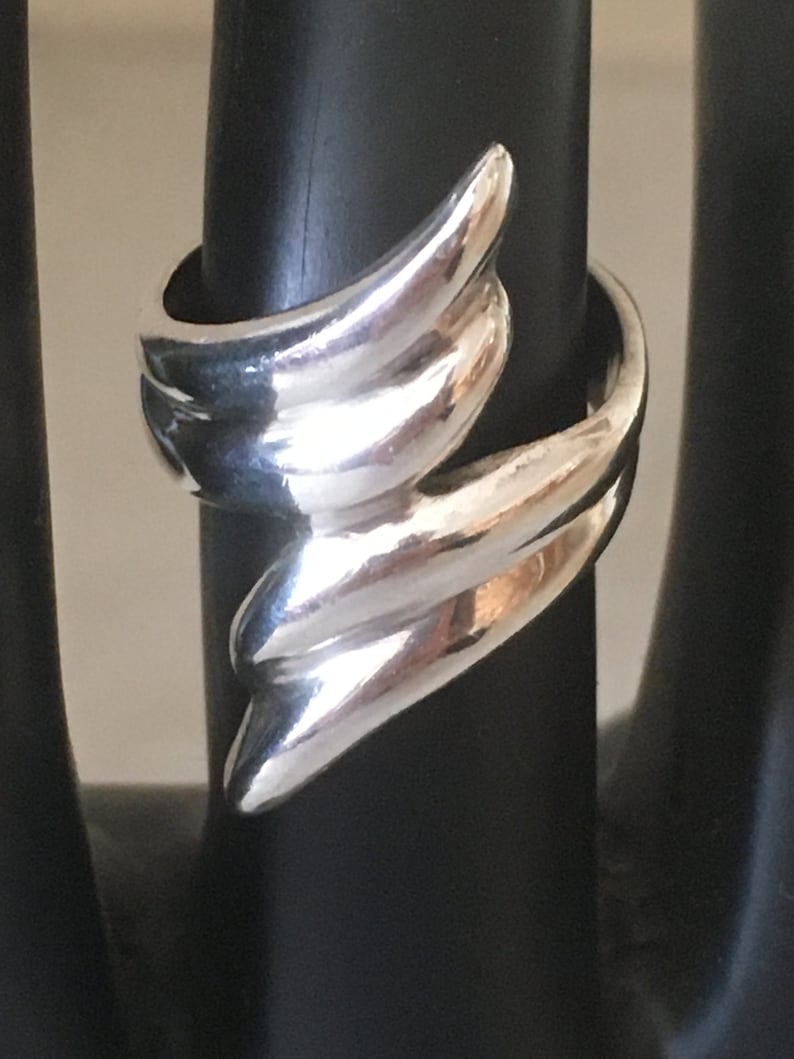 May include: A silver ring with a unique, abstract design. The ring is made of smooth, polished metal and has a modern, minimalist style.