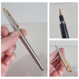 May include: A silver and gold-tone pen with a sleek design. The pen features a gold clip and accents, with a silver body. The pen's tip is also gold. The pen is held in a hand.