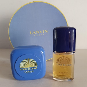Puede incluir: Un conjunto de perfume vintage con una caja azul y un frasco de "Clair de Jour" de Lanvin Paris. El frasco tiene una tapa azul oscuro y una etiqueta dorada. La caja redonda es azul claro con el logotipo de Lanvin Paris.