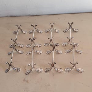May include: A set of silver-coloured decorative stands. Each stand features a central vertical support with ornate, curved arms. The stands are arranged in rows, possibly for display or serving purposes.