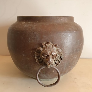 May include: A large, round, copper planter with a lion head handle and a ring.