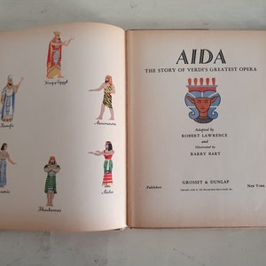May include: A book cover with the title "AIDA THE STORY OF VERDI'S GREATEST OPERA" and illustrations of characters from the opera. The cover is beige with a red and gold design.