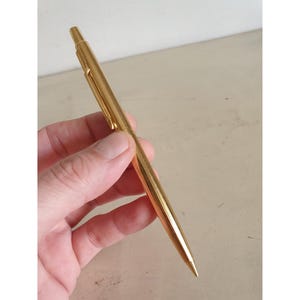 Könnte beinhalten: Ein goldfarbener mechanischer Bleistift mit einem schlanken, zylindrischen Design.