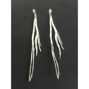 Puede incluir: Un par de pendientes largos de plata con un diseño delicado en forma de rama. Los pendientes están hechos de alambre fino de plata que se tuerce y se da forma para crear un patrón único e intrincado.