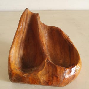 May include: A wooden bowl with two carved out sections. The bowl is a light brown colour and has a rough, natural texture.