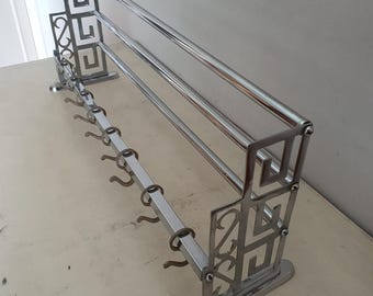 May include: Chrome-plated metal coat rack with two horizontal bars and multiple hooks. The rack has an Art Deco design with geometric patterns.