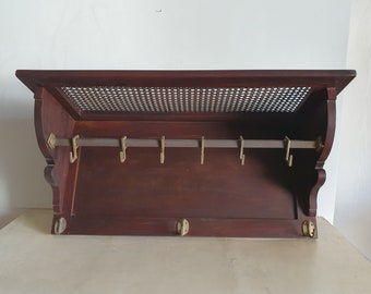 May include: A dark wood wall mounted coat rack with a woven cane shelf and brass hooks.