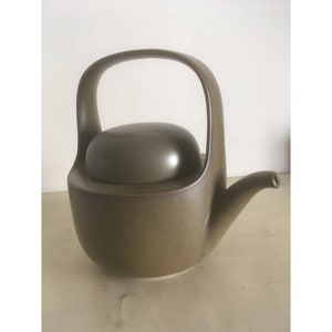 Könnte beinhalten: Eine braune Teekanne aus Keramik mit Deckel und gebogenem Griff. Die Teekanne hat eine gesprenkelte Oberfläche.