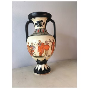 Può includere: Un vaso in ceramica bianco e nero con una scena di persone e un calderone dipinti in arancione sul davanti. Il vaso ha una base nera e un bordo nero.