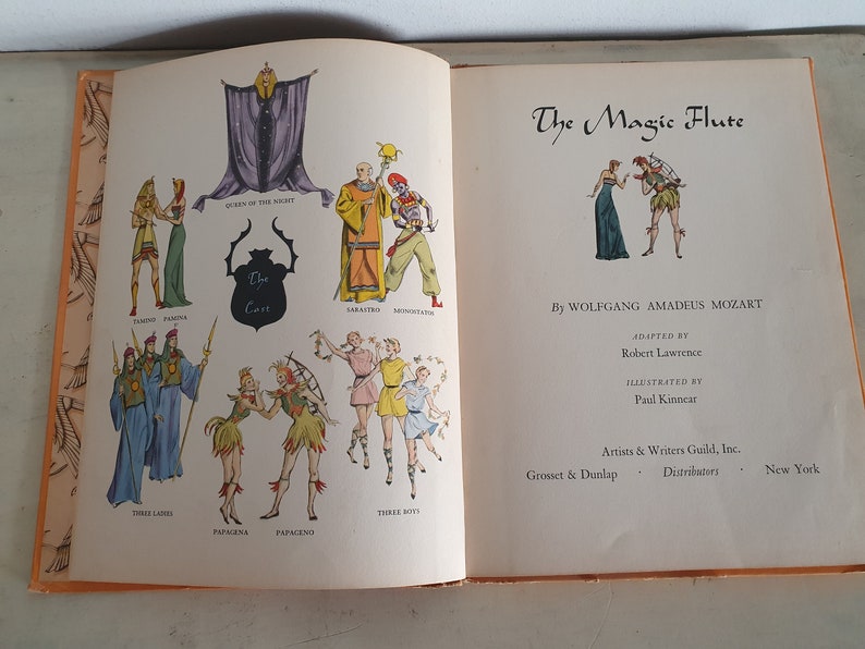May include: An illustrated book cover for a children's adaptation of The Magic Flute opera by Wolfgang Amadeus Mozart. The cover features a colorful cast of characters from the opera, including the Queen of the Night, Sarastro, and Papagena.