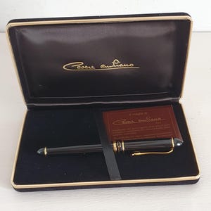 Könnte beinhalten: Ein schwarzer Cesare Emiliano Füllfederhalter mit goldenen Akzenten, präsentiert in einer schwarzen, samtgefütterten Box. Die Box hat einen goldenen Rand und das Cesare Emiliano Logo. Eine kleine Karte ist sichtbar.