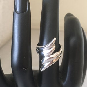 May include: A silver ring with a unique, abstract design. The ring is made of smooth, polished metal and has a modern, geometric shape.