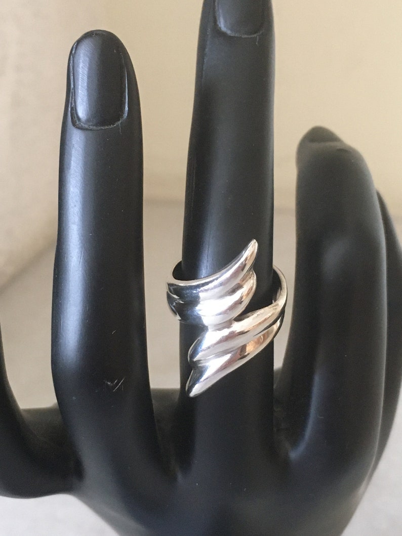 May include: A silver ring with a unique, abstract design. The ring is made of smooth, polished metal and has a modern, geometric shape.