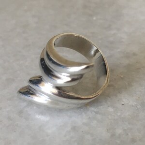 May include: A silver ring with a unique, abstract design. The ring is made of smooth, curved lines that create a flowing, organic shape.